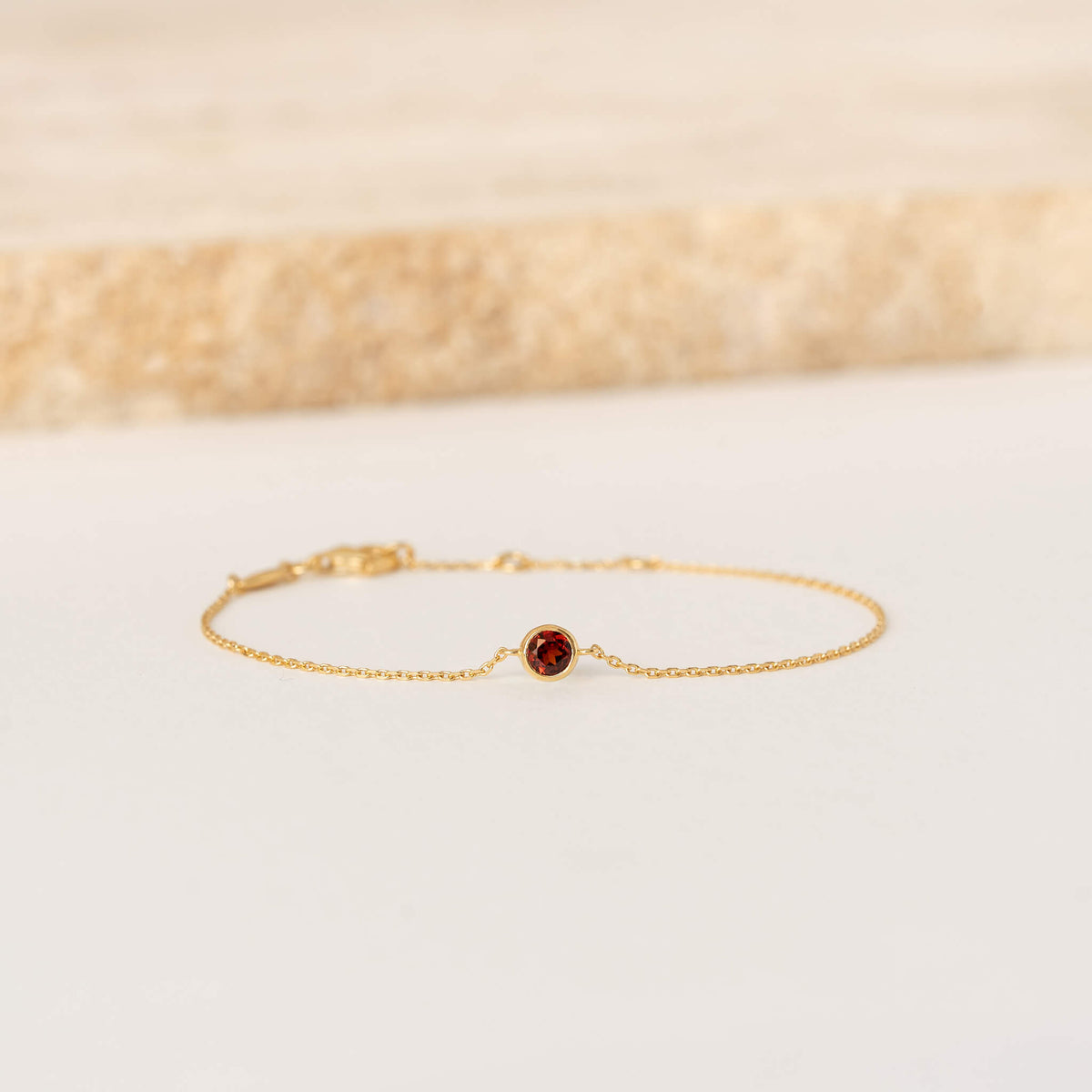 Delicate Gold Vermeil chain bracelet featuring a small round Garnet gemstone centerpiece, laid flat on a light-colored surface.