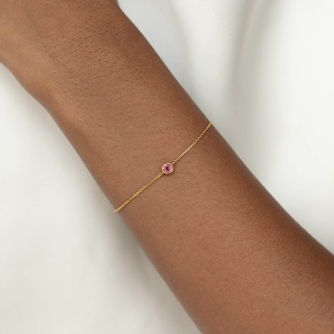 Delicate Gold Vermeil chain bracelet with a small round Dark pink tourmaline gemstone centerpiece, worn around a woman's wrist.