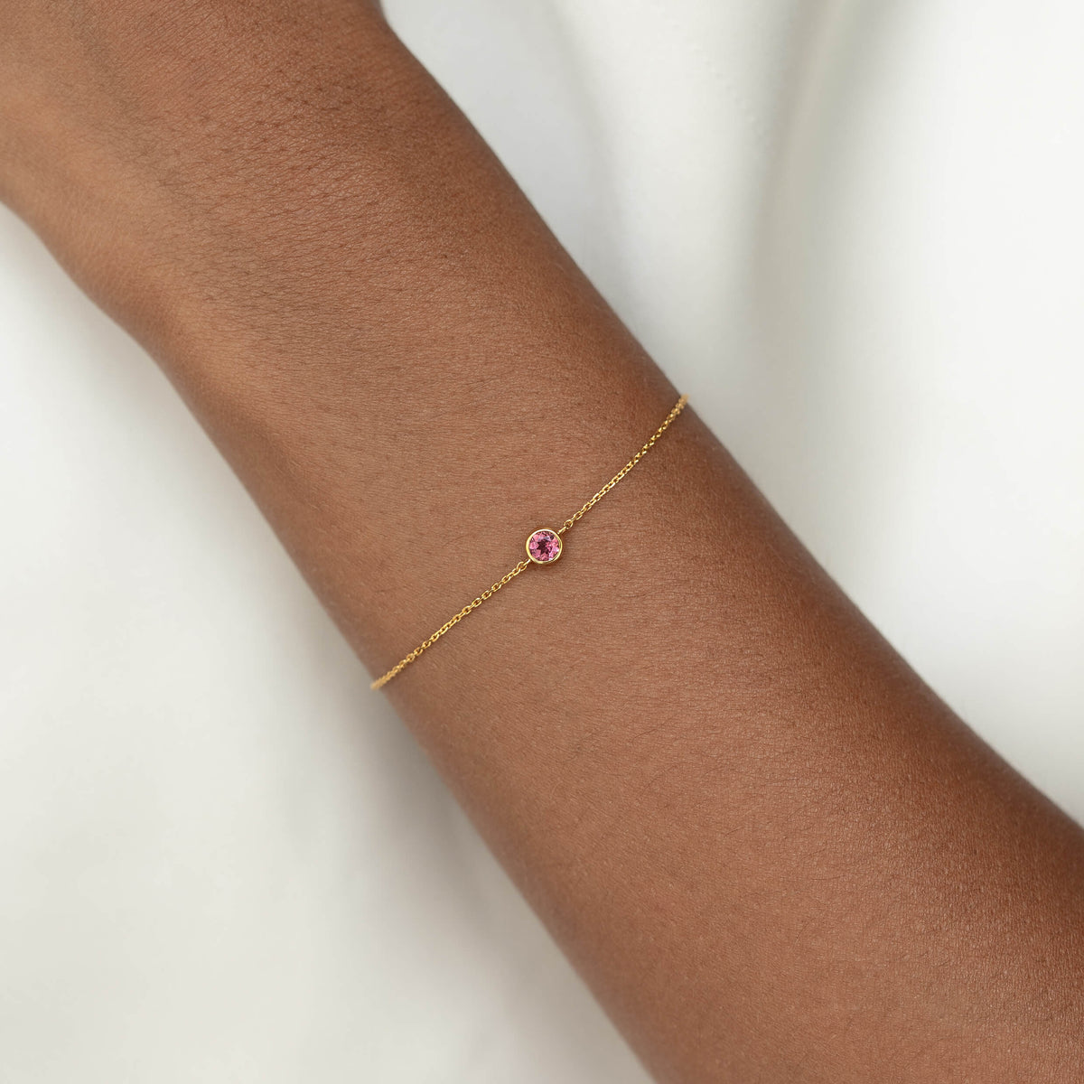 Delicate Gold Vermeil chain bracelet with a small round Dark pink tourmaline gemstone centerpiece, worn around a woman's wrist.