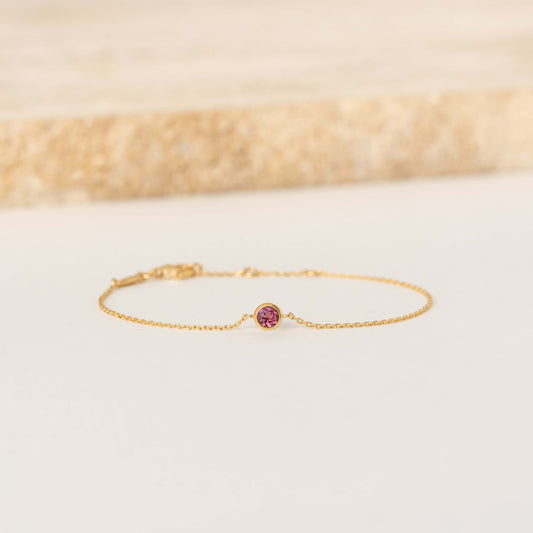 Delicate Gold Vermeil chain bracelet featuring a small round Dark pink tourmaline gemstone centerpiece, laid flat on a light-colored surface.