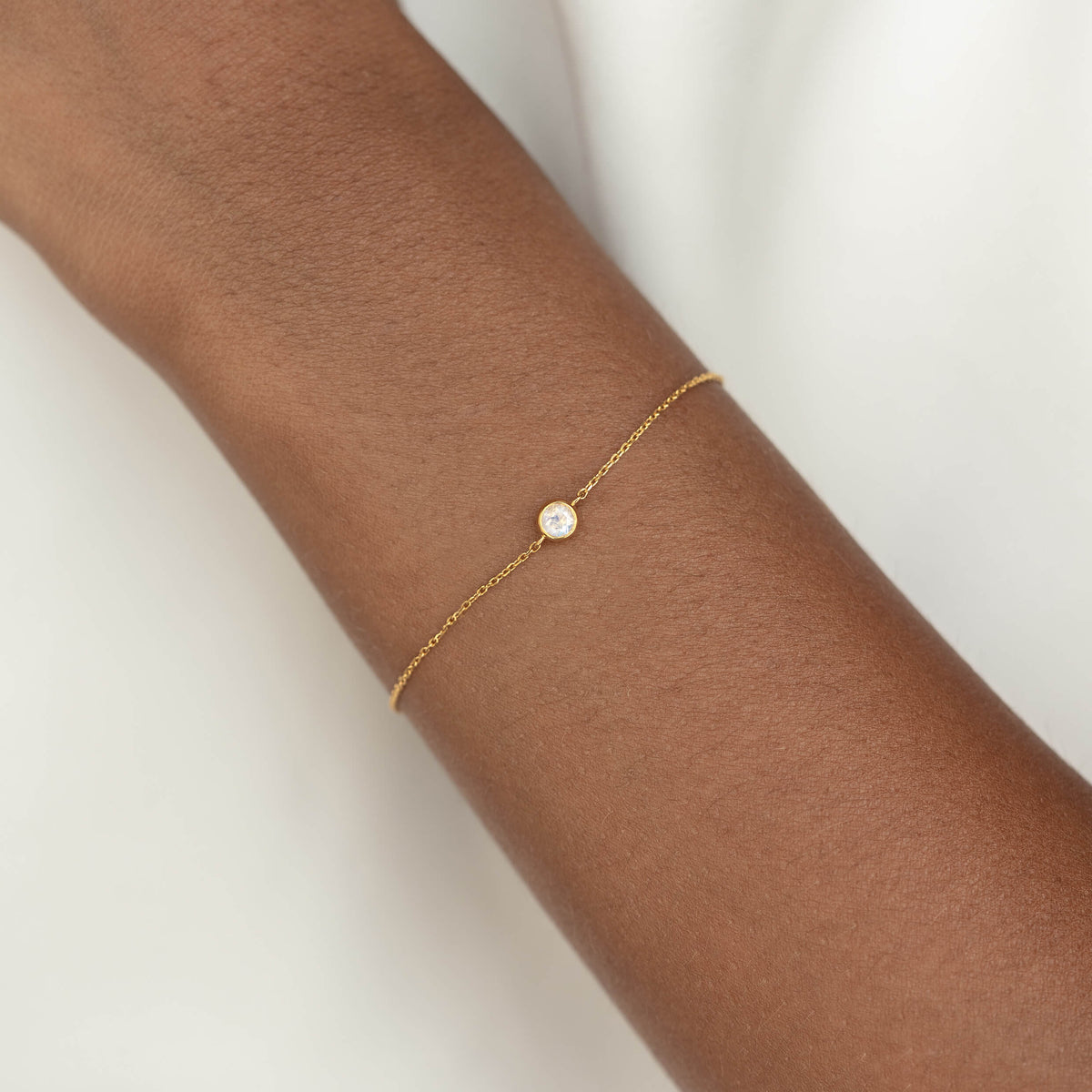 Delicate Gold Vermeil chain bracelet with a small round Moonstone gemstone centerpiece, worn around a woman's wrist.