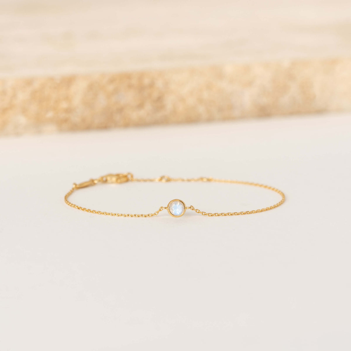 Delicate Gold Vermeil chain bracelet featuring a small round Moonstone gemstone centerpiece, laid flat on a light-colored surface.