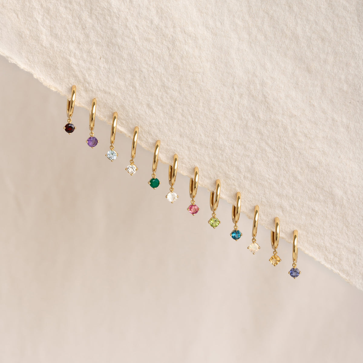 Close-up of multiple gold vermeil drop huggie earrings featuring various birthstones including June Birthstone Drop Huggie Earrings - Moonstone
