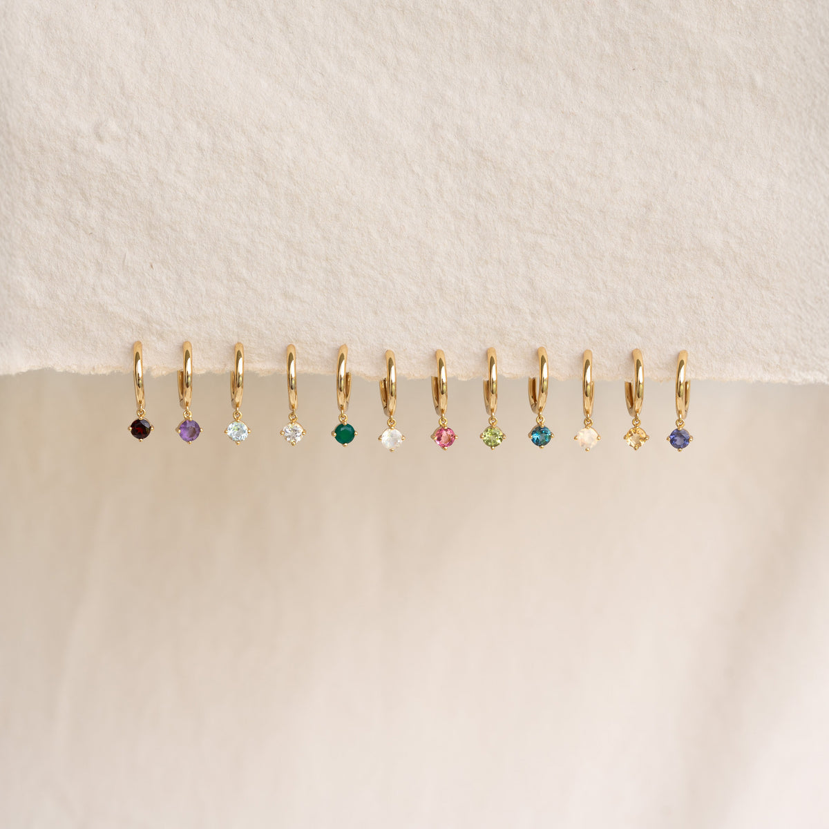 Row of delicate gold drop huggie earrings featuring various gemstones including June Birthstone Drop Huggie Earrings Moonstone