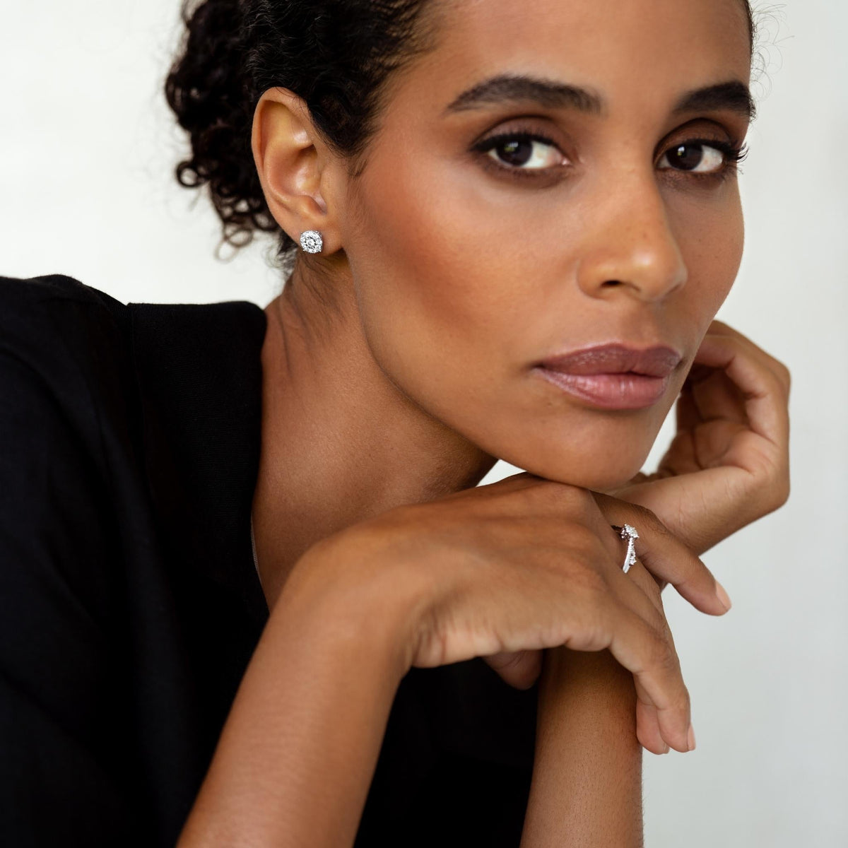 Close-up of a woman wearing Diamond Earrings - 2 Carat Miracle Plate with a black top on a neutral background
