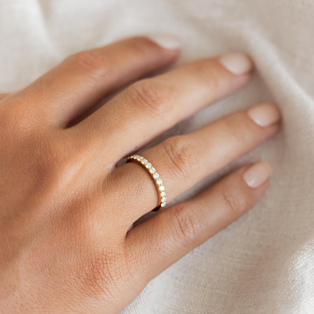 Close-up of a hand wearing the Diamond Half Eternity Ring 14k Gold - Isa on a soft neutral fabric background