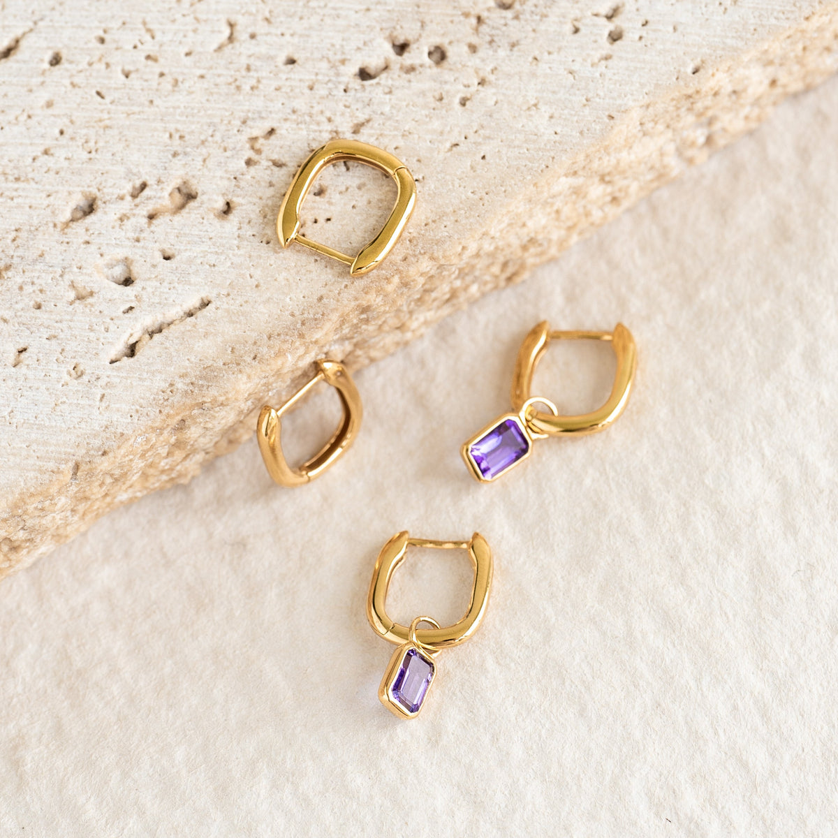 Square Huggie Earrings - Amelia in gold vermeil with small purple gemstone dangles on a neutral textured background