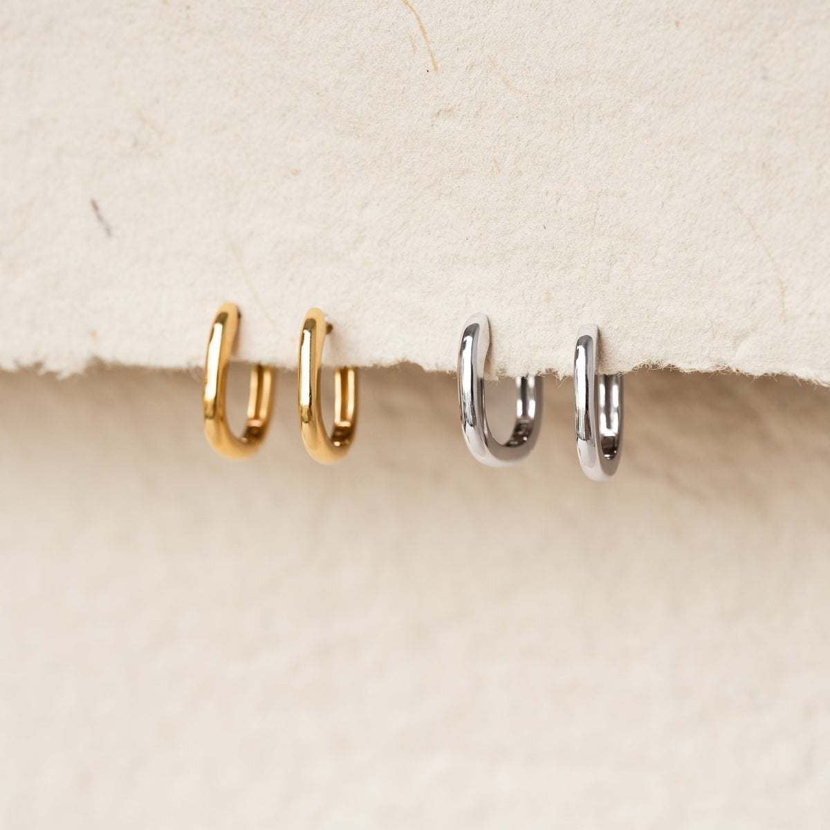 Square Huggie Earrings - Amelia in gold vermeil and silver displayed on a textured beige background