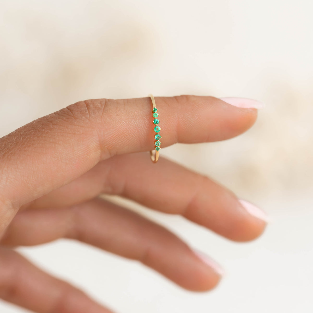 Close-up of a hand wearing the Graduated Emerald Ring 14k Gold - Mila featuring seven round emeralds on a gold band
