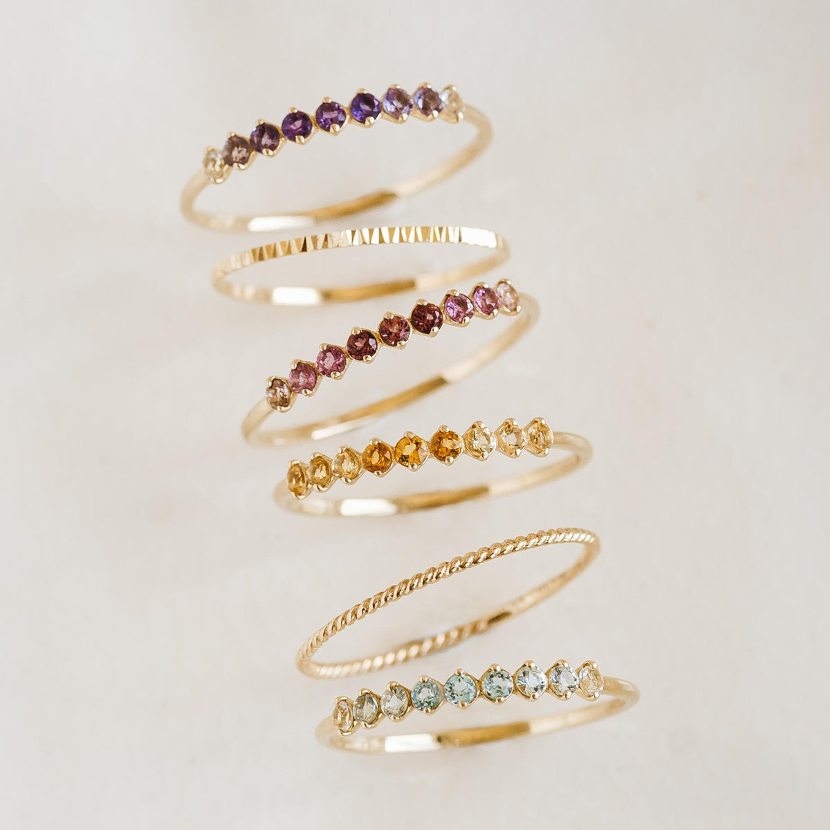 Stack of delicate 14k gold rings featuring February Birthstone Ring 14k Gold - Ombre Amethyst and other gemstones on a neutral background