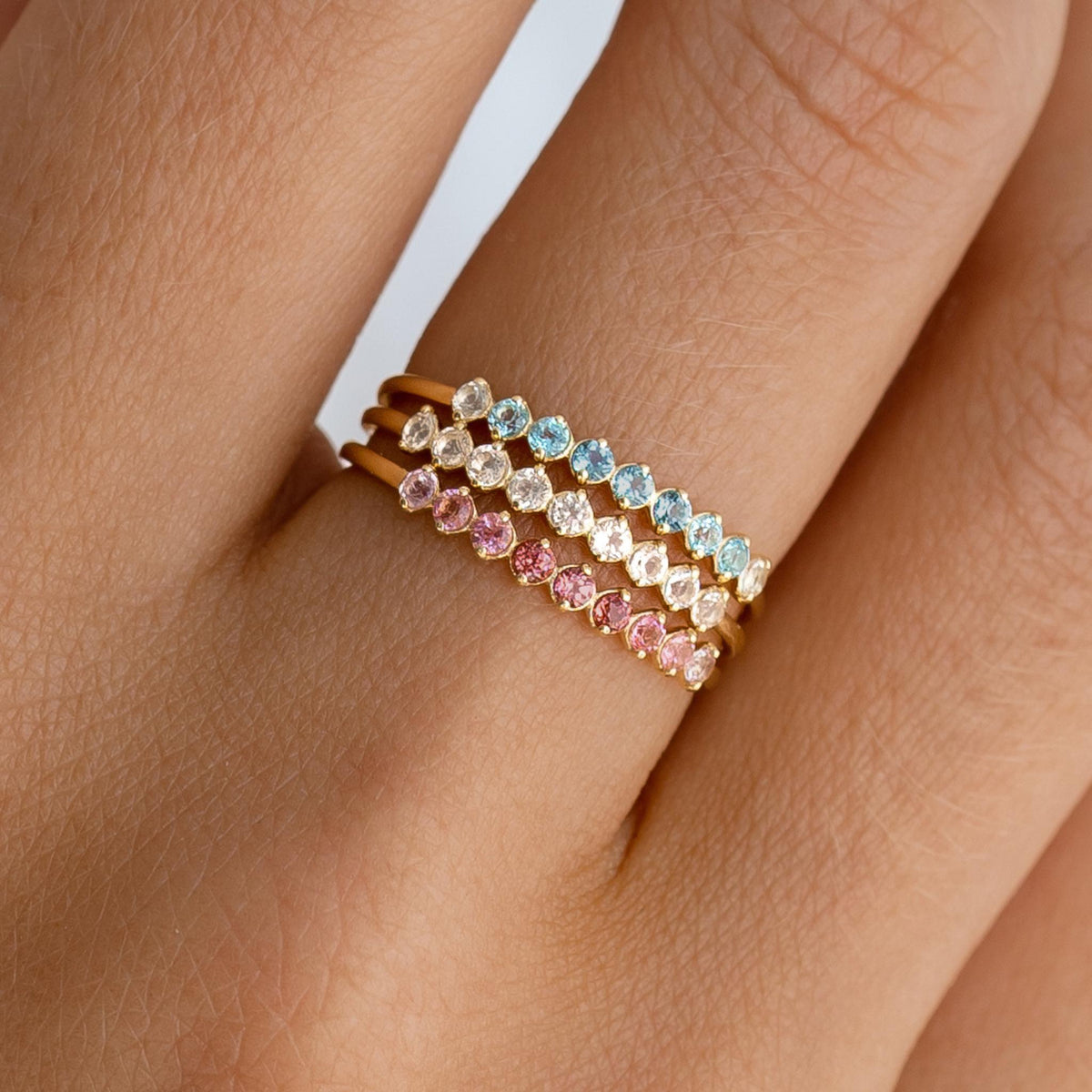Close-up of a hand wearing three September Birthstone Ring 14k Gold - Ombre London Blue Topaz rings with blue, white, and pink stones