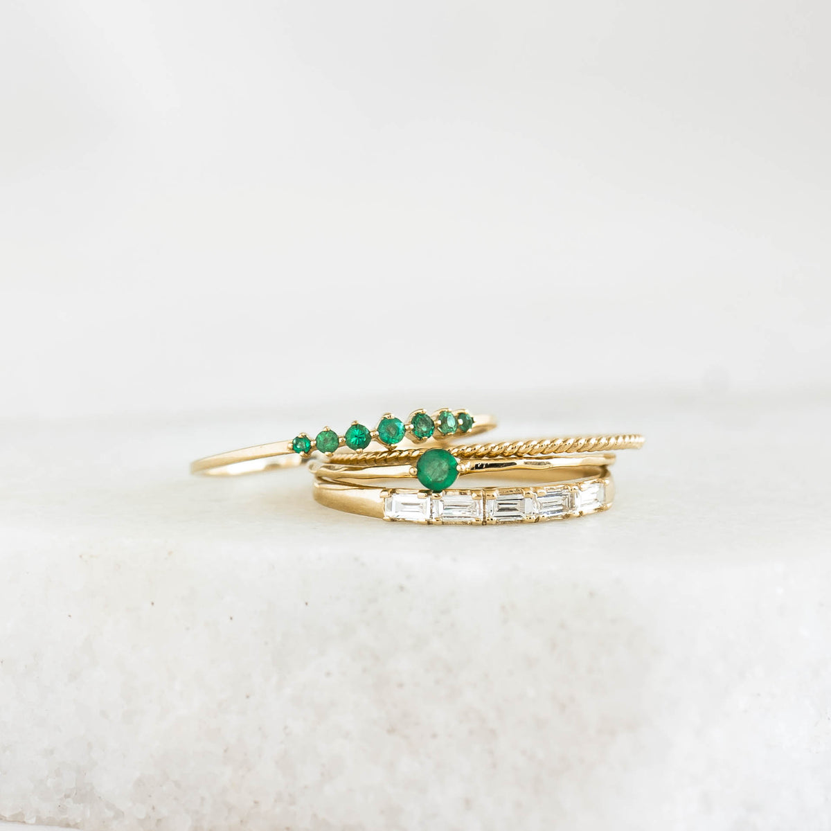 Graduated Emerald Ring 14k Gold - Mila with seven round emeralds in varying sizes on a white stone surface