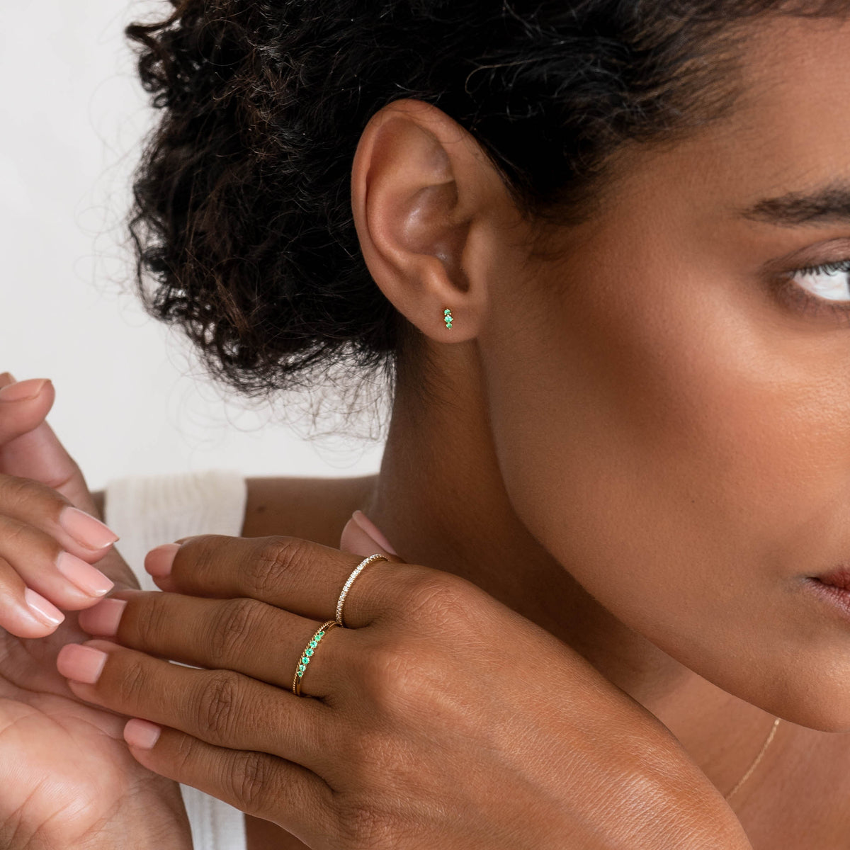 Close-up of woman wearing the Graduated Emerald Ring 14k Gold - Mila with matching emerald stud earrings on a white background