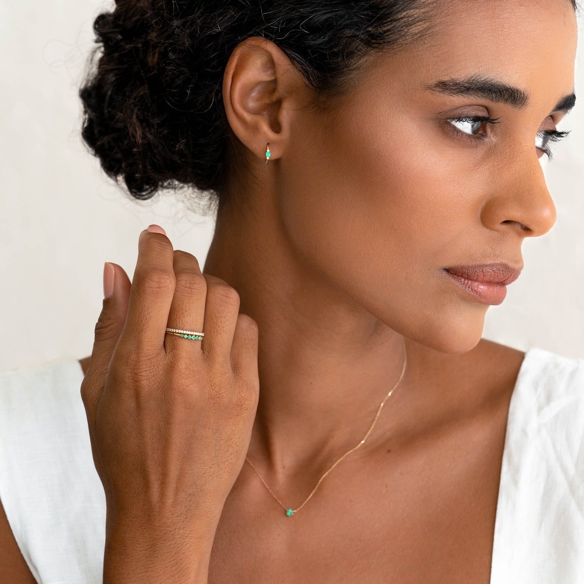 Close-up of woman wearing Graduated Emerald Ring 14k Gold - Mila with matching emerald earrings and necklace on white top