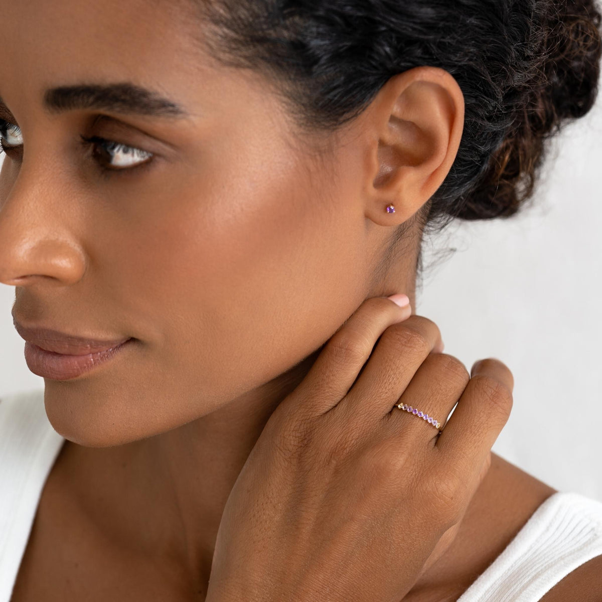 Close-up of a woman wearing February Birthstone Stud Earrings 14k Gold - Amethyst with a white top on a neutral background