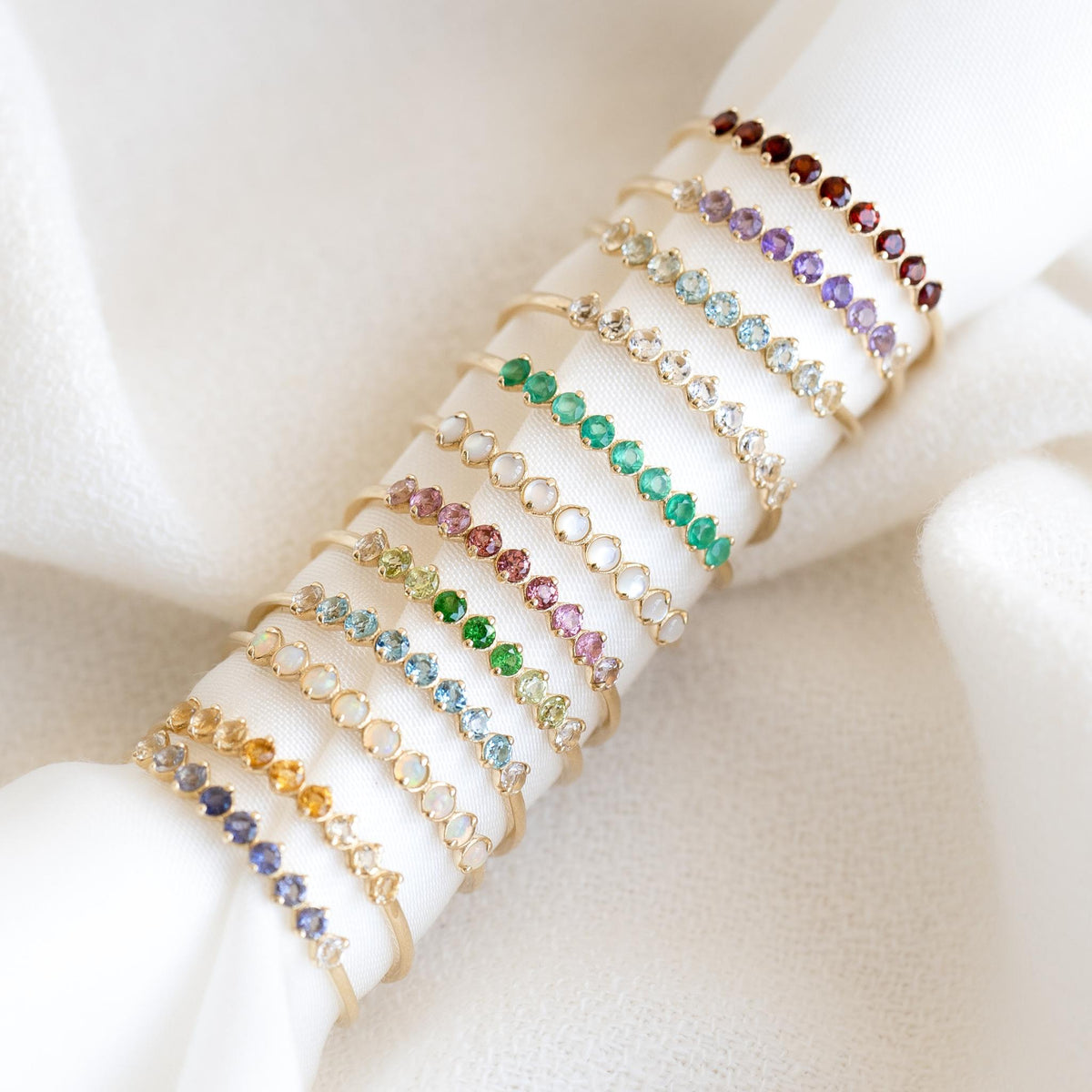 Stack of delicate September Birthstone Ring 14k Gold - Ombre London Blue Topaz and other gemstone rings on white fabric background