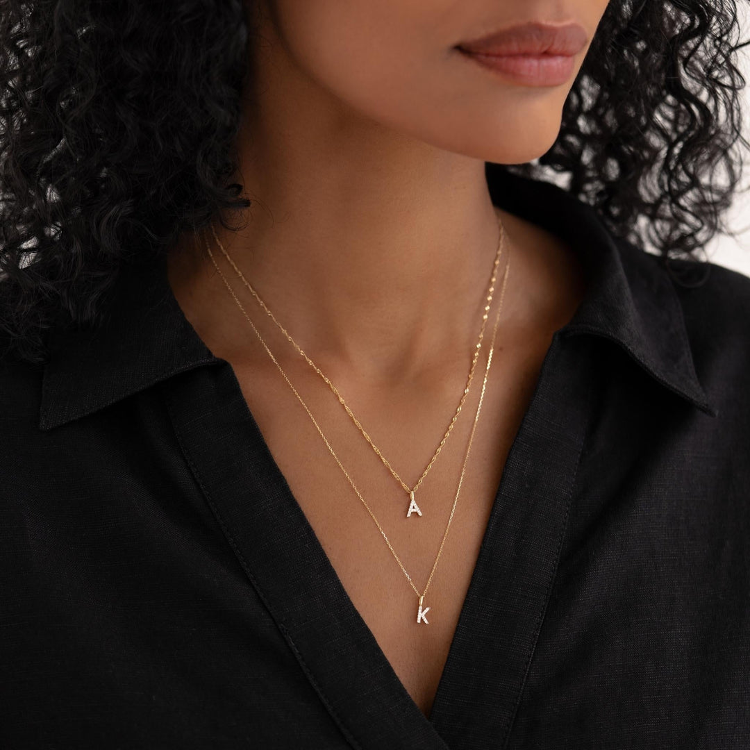 Close-up of a woman wearing layered Diamond Initial Pendant 14k Gold - K and A necklaces with a black top