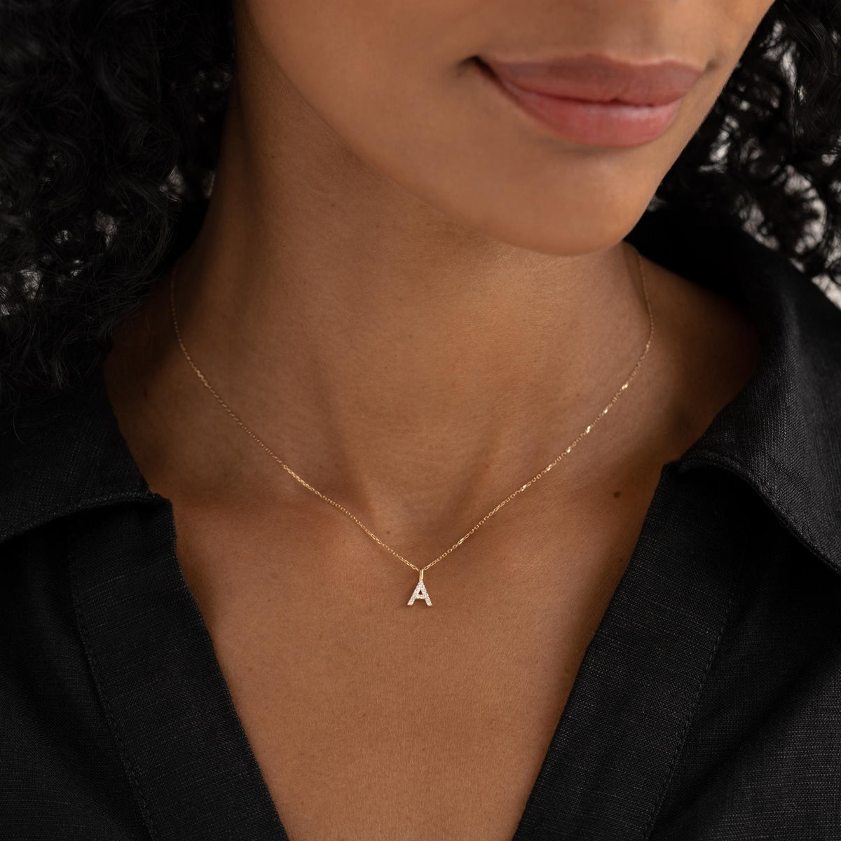 Close-up of woman wearing a Diamond Initial Pendant 14k Gold - P on a delicate gold chain with a black top