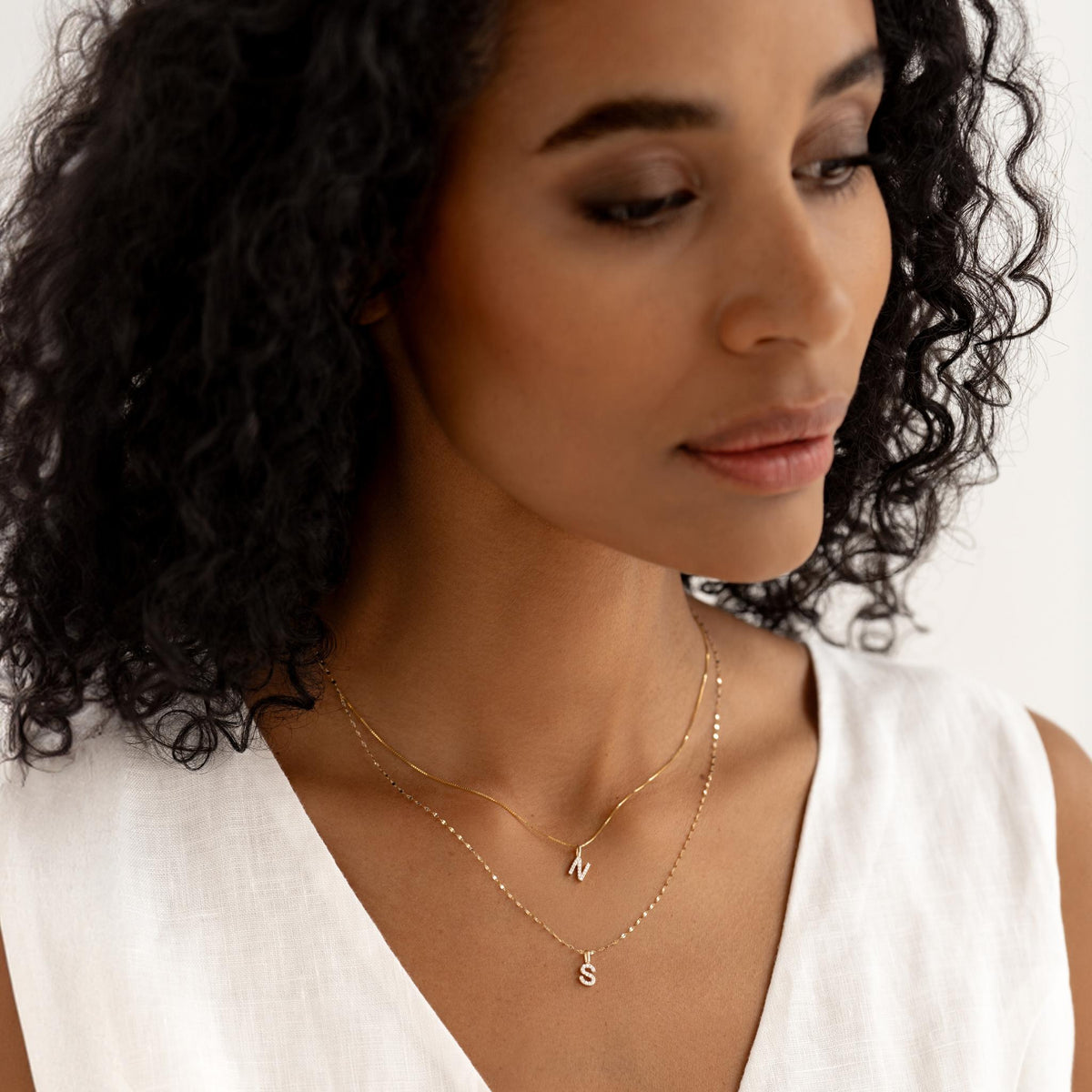 Close-up of woman wearing layered Diamond Initial Pendant 14k Gold - C and N necklaces with a white linen top