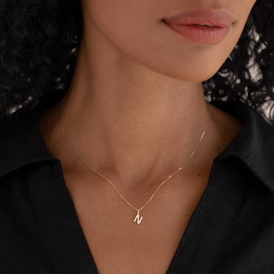 Close-up of woman wearing Diamond Initial Pendant 14k Gold - N on a delicate gold chain with a black top