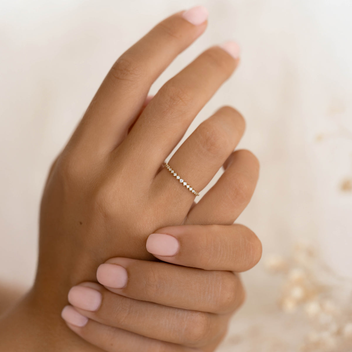 Close-up of hand wearing a delicate Graduated Diamond Ring 14k Gold - Ophelia with 15 sparkling diamonds on a neutral background