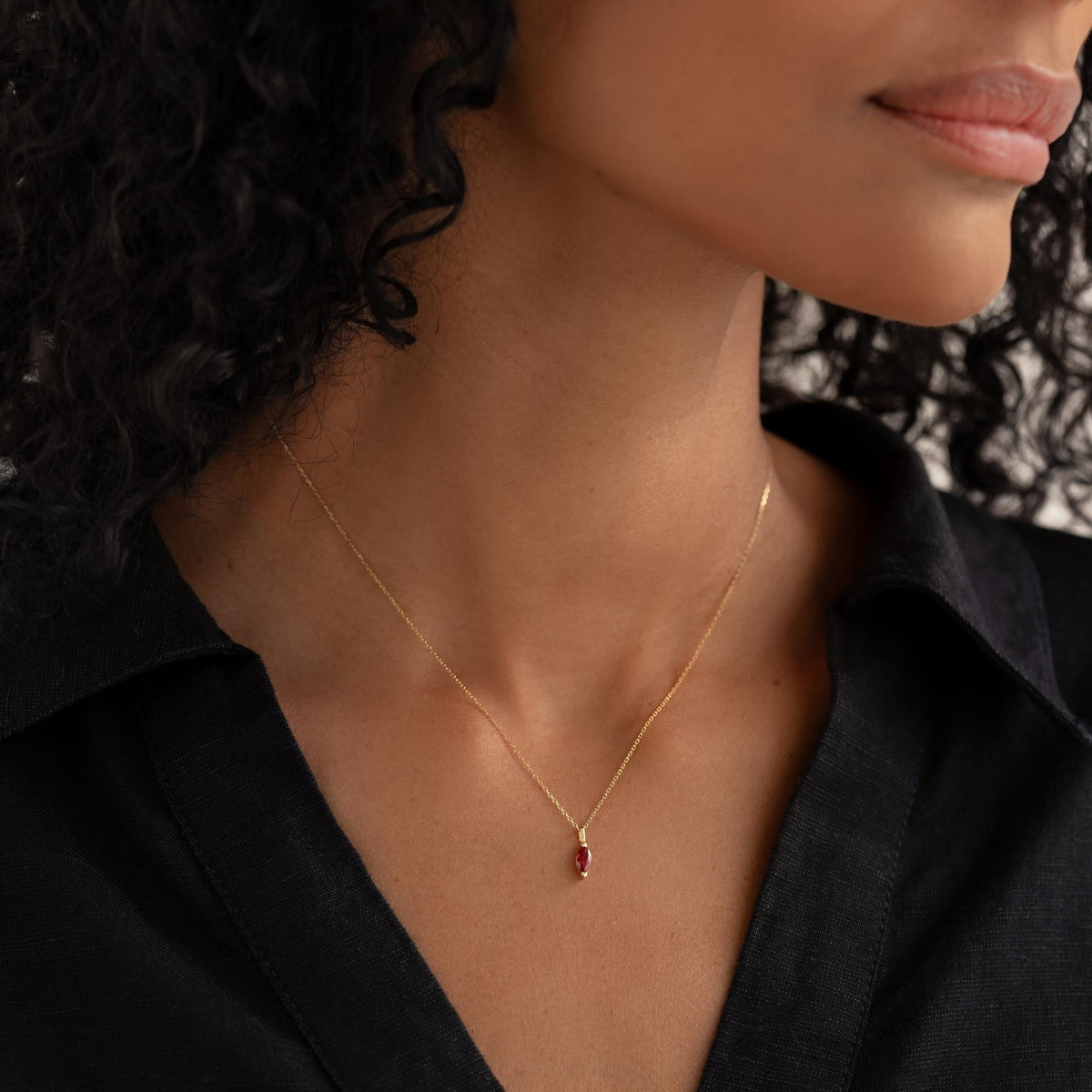 Close-up of a woman wearing the January Birthstone Pendant 14k Gold - Garnet with a black collared shirt