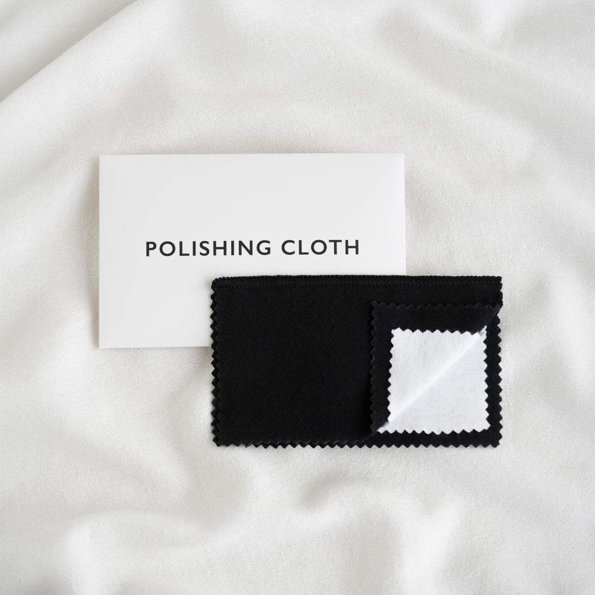 Jewelry Polishing Cloth with black and white layers displayed on soft white fabric background