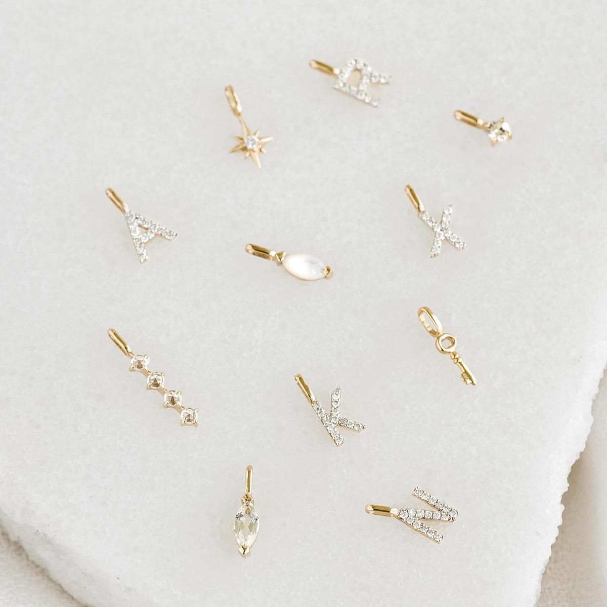 Heart Charm 14k Gold along with assorted delicate gold and diamond letter and shape charms on a light background