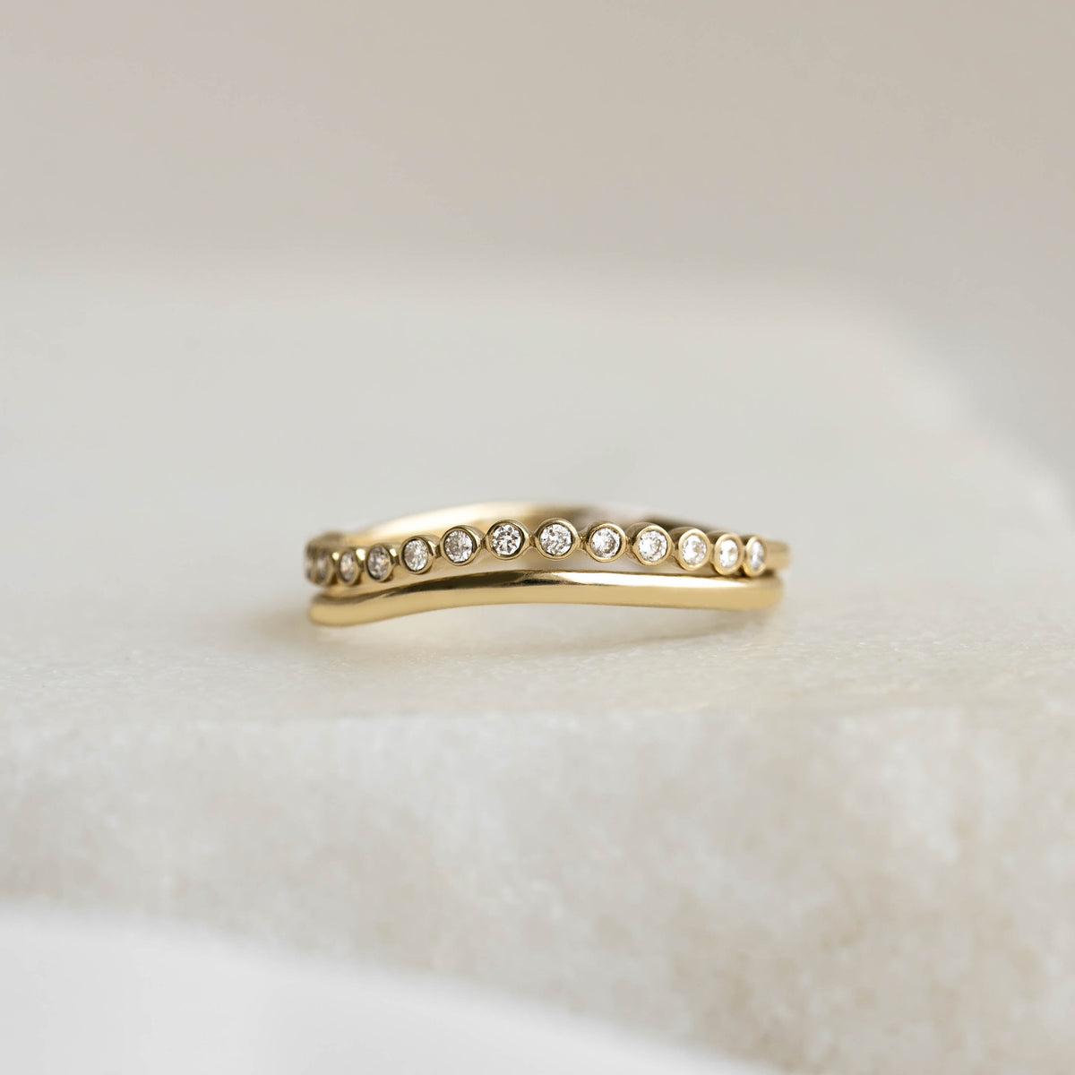 Close-up of the Wavy Ring 14k Gold - Brielle featuring small diamonds set along the wavy band on a soft neutral background