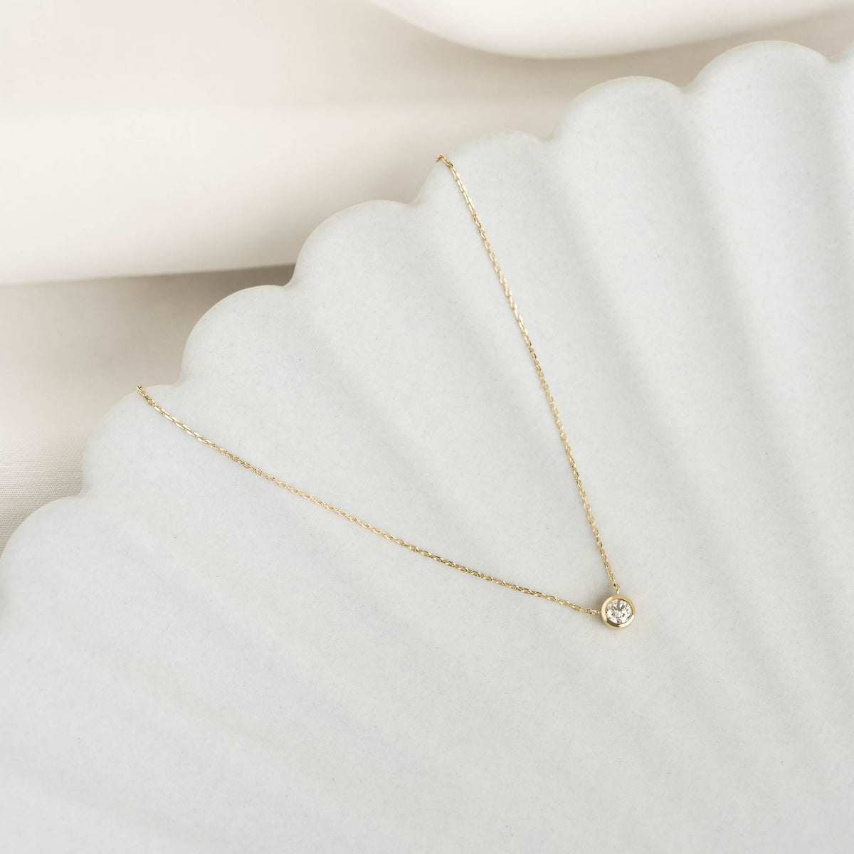 Gold necklace with a small round pendant on a white textured surface