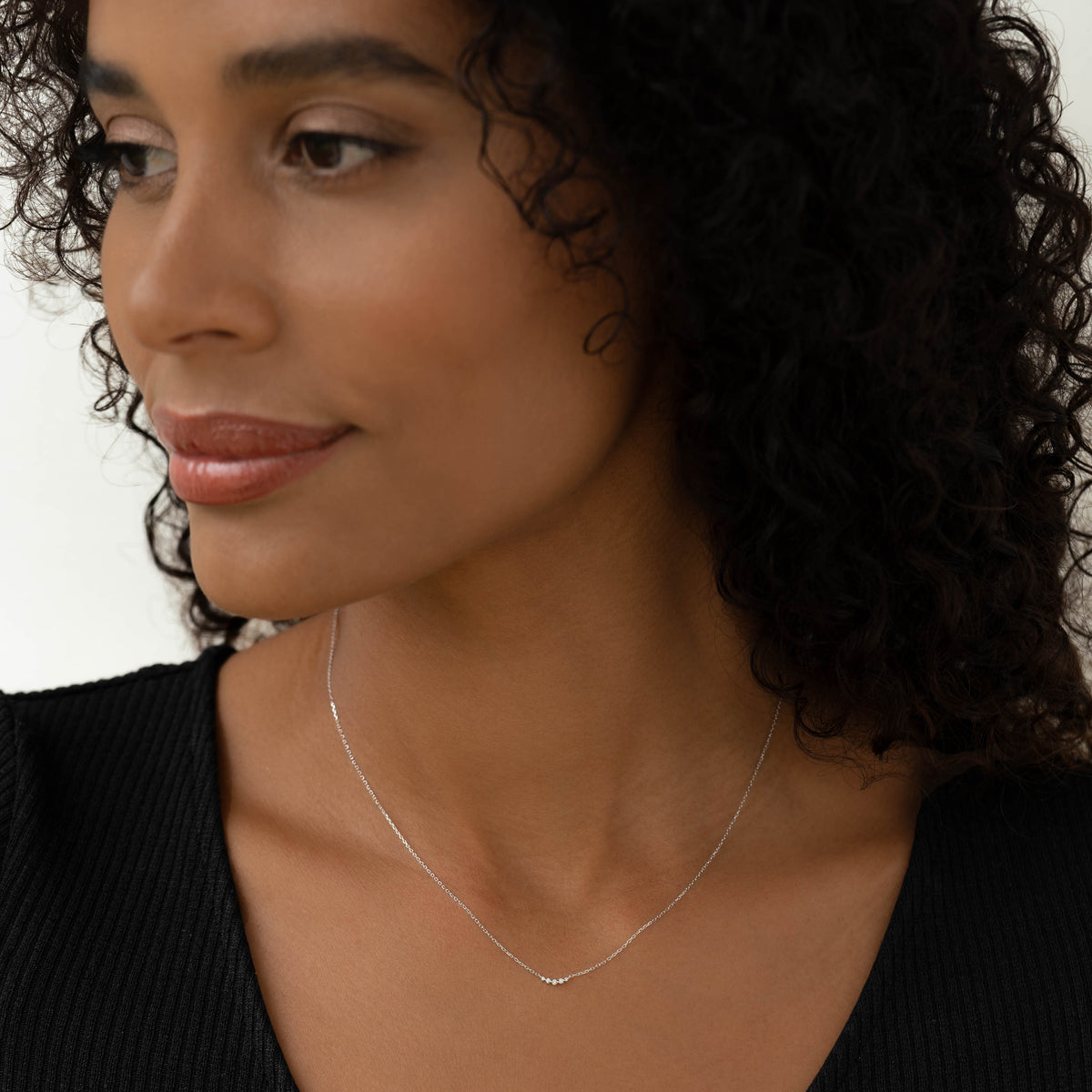 Close-up of woman wearing Diamond Curved Bar Necklace White Gold - Jemma with five small diamonds on a delicate chain