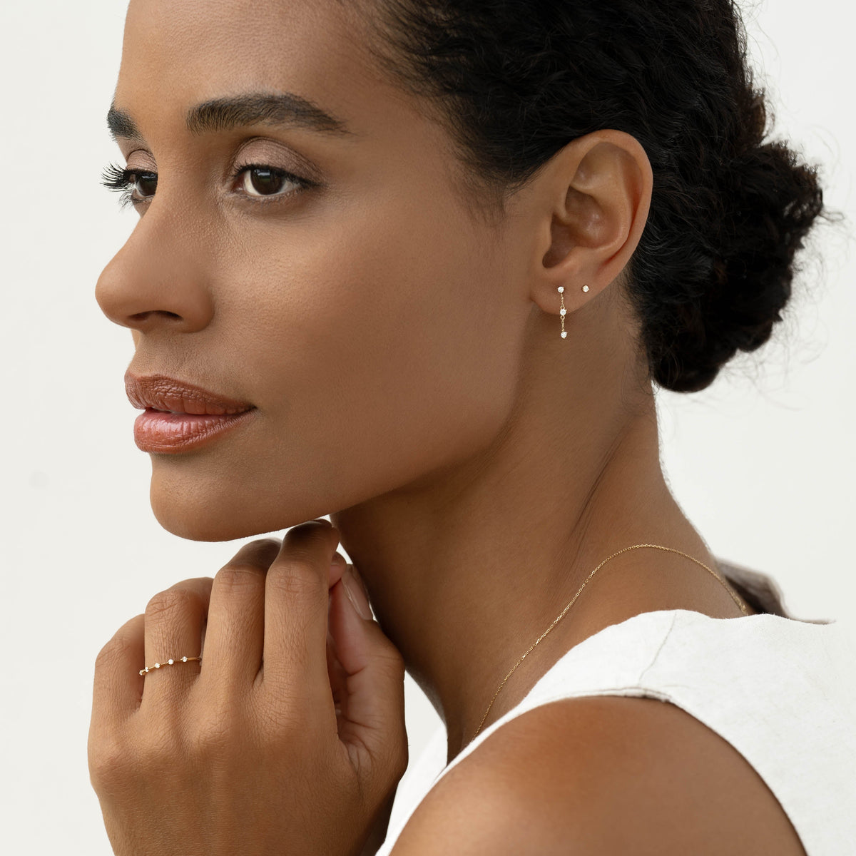 Close-up of woman wearing Diamond Drop Earrings 14k Gold - Alessia with a white sleeveless top on a neutral background