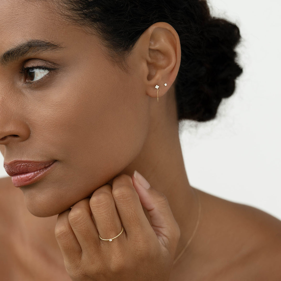 Close-up of woman wearing Diamond Chain Earrings 14k Gold - Alva with delicate gold ring on a neutral background