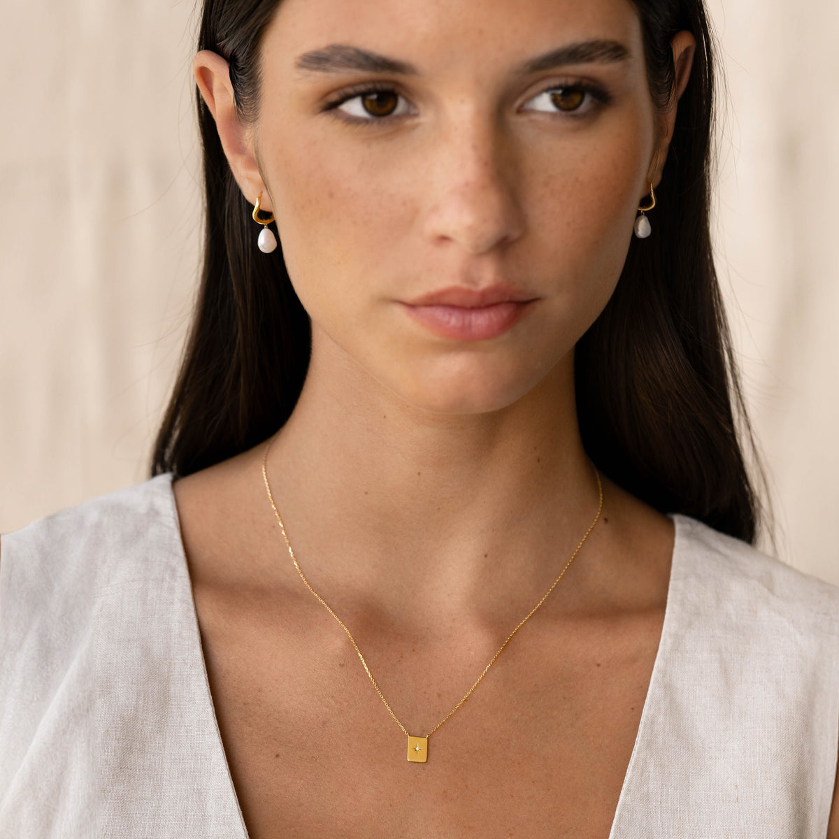 Close-up of a woman wearing a Diamond Star Necklace - Polaris with a gold tag pendant featuring a central diamond on a light backdrop