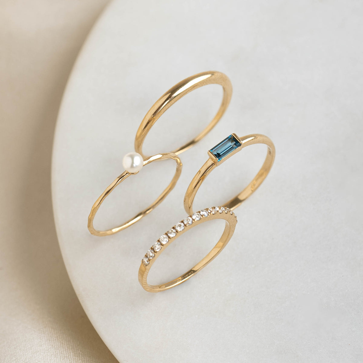 Close-up of Baguette Ring London Blue Topaz 14k Gold - Synne with pearl and diamond stack on marble surface