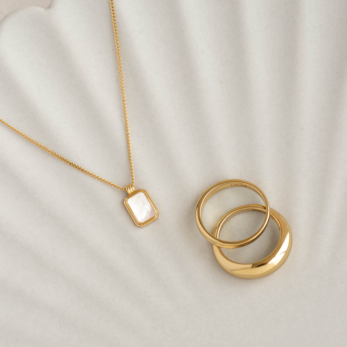 Mother of Pearl Tag Necklace - Iria with gold vermeil chain displayed next to three gold rings on neutral background