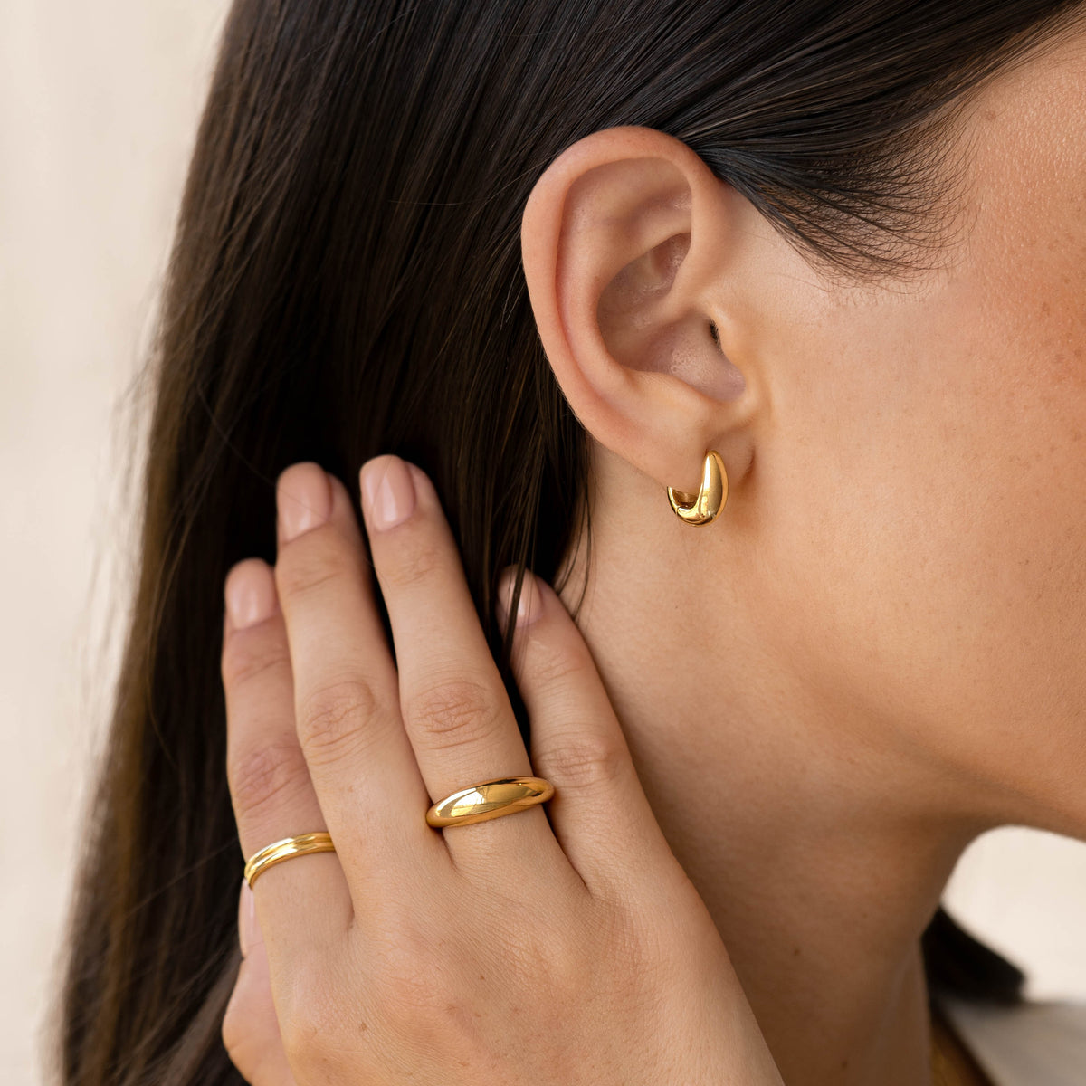 Close-up of a woman wearing Dome Huggie Earrings - Caja in gold vermeil with matching gold rings on fingers