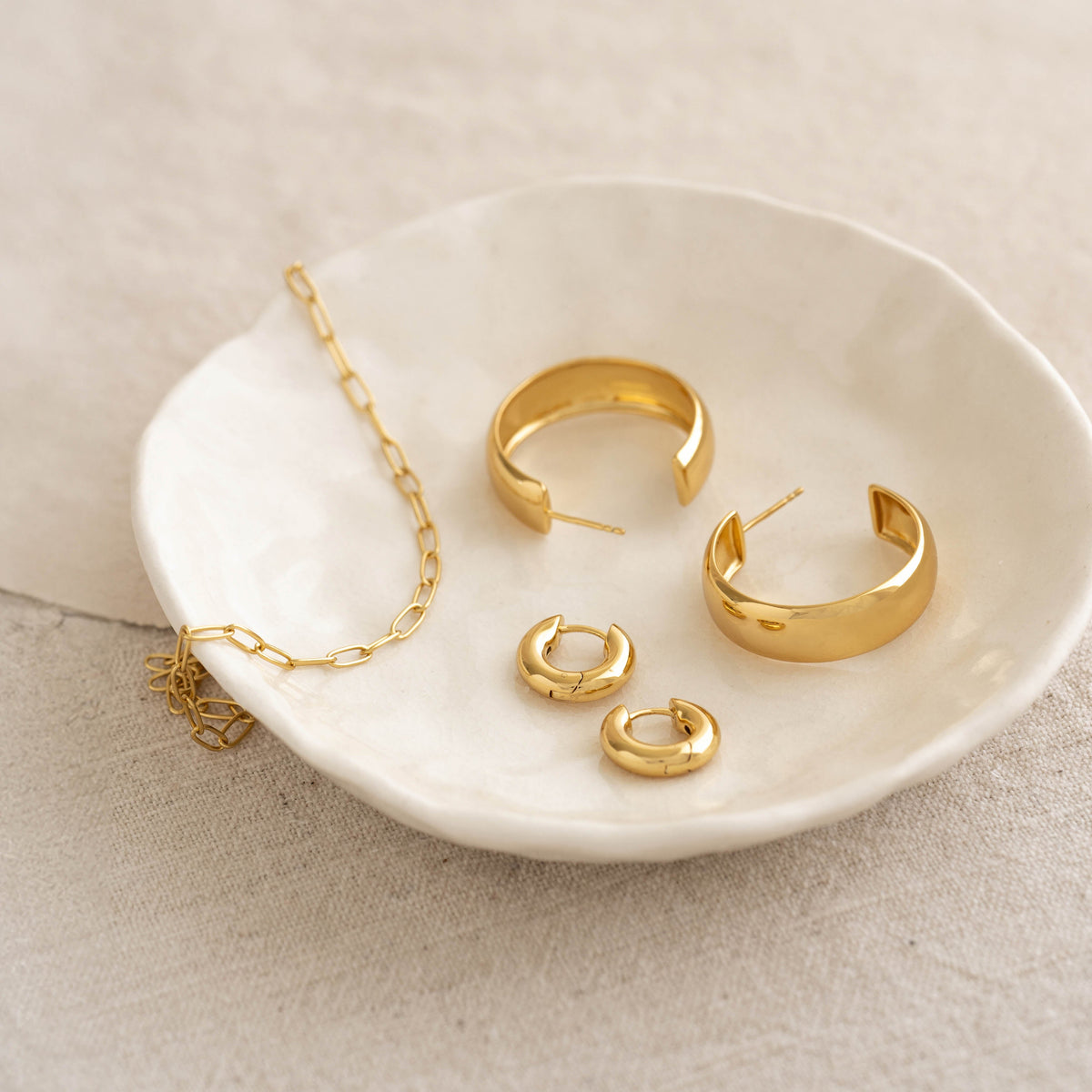 Chain Link Necklace 14k Gold with varying sized gold hoop earrings displayed on a white ceramic dish