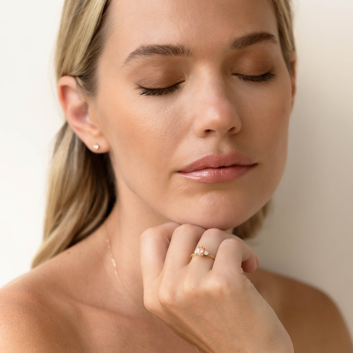 Woman with closed eyes wearing Morganite and Diamond Ring Rose Gold - Kindra on her finger against a neutral background