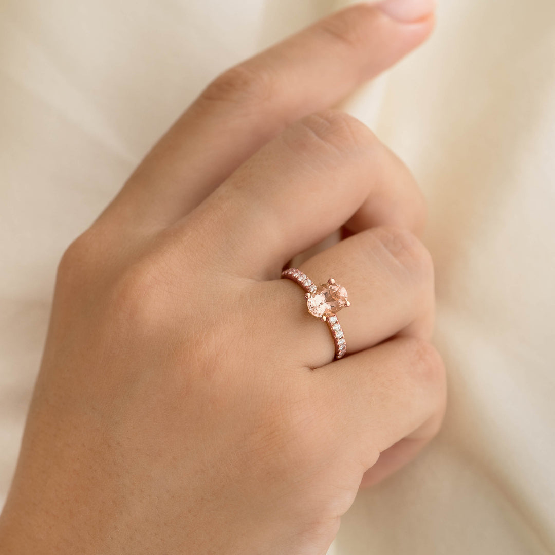 Hand wearing Oval Morganite and Diamond Ring Rose Gold - Minette with pavé diamonds on a soft beige background
