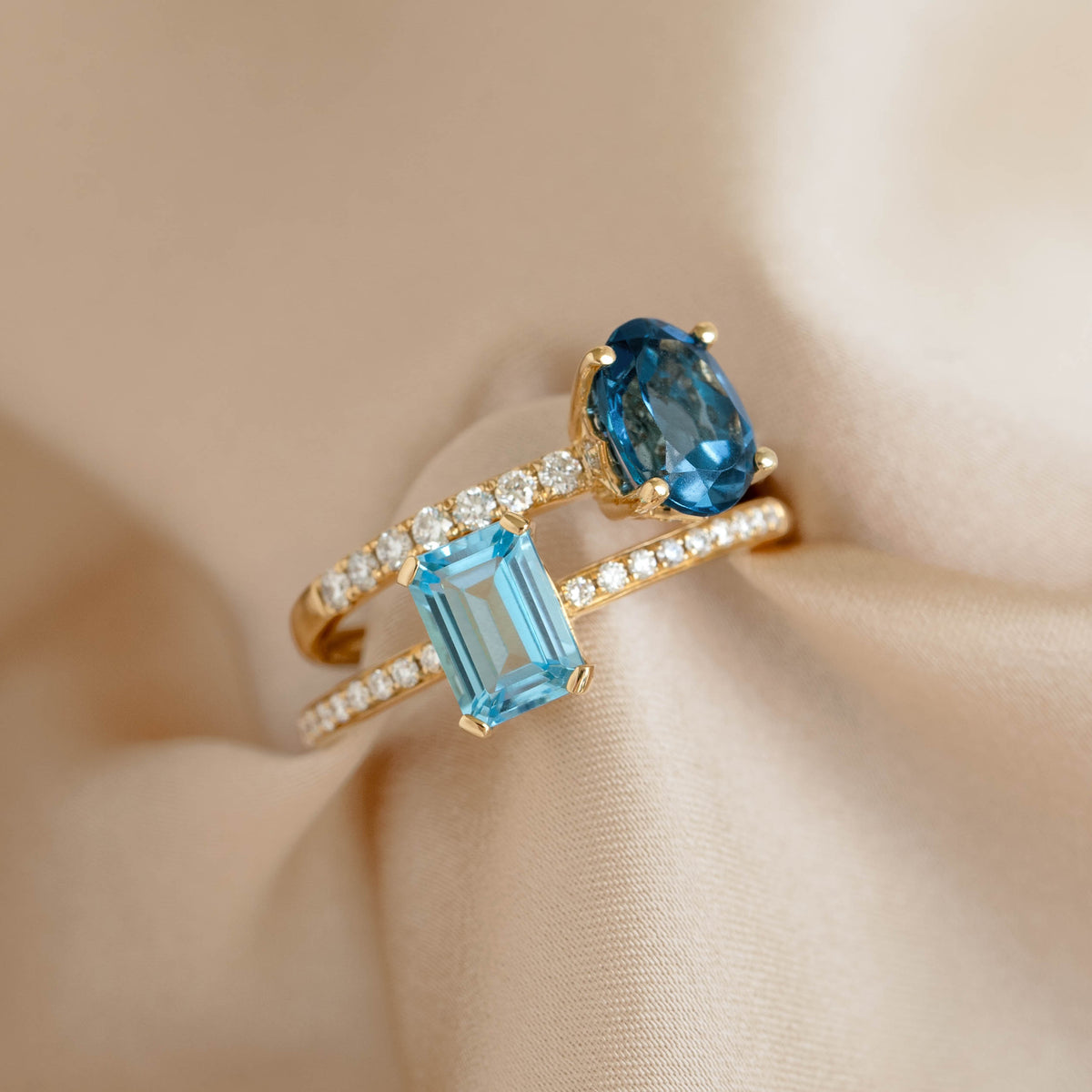 Close-up of Oval London Blue Topaz and Diamond Ring 14k Gold - Minette with two blue gemstones and pavé diamonds on fabric background