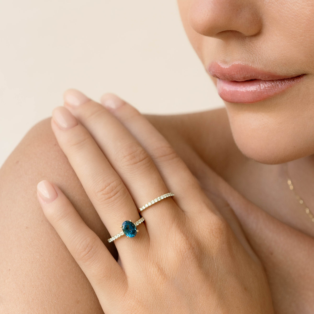 Close-up of a hand wearing the Oval London Blue Topaz and Diamond Ring 14k Gold - Minette on a neutral background