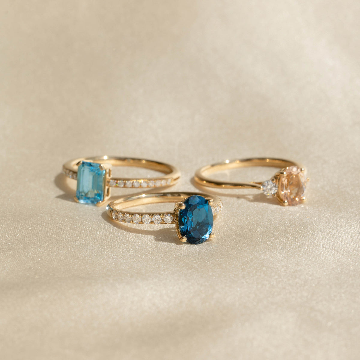 Three gold rings with oval gemstones including the Oval London Blue Topaz and Diamond Ring 14k Gold - Minette on a soft beige background