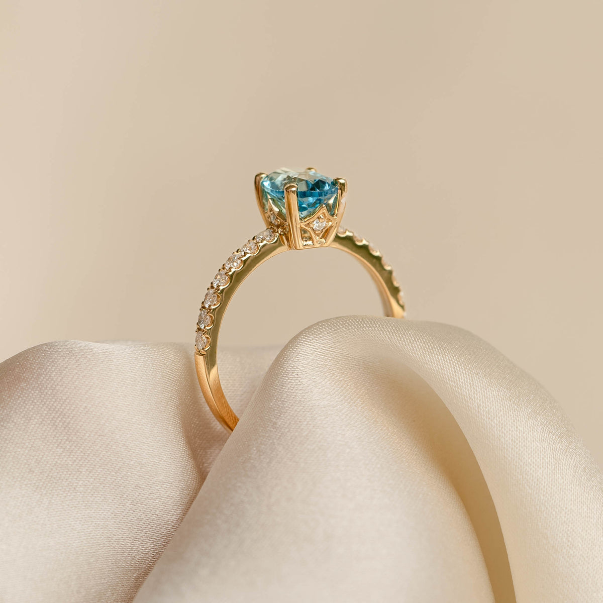 Oval Swiss Blue Topaz and Diamond Ring 14k Gold - Minette with pavé diamonds on band displayed on cream fabric