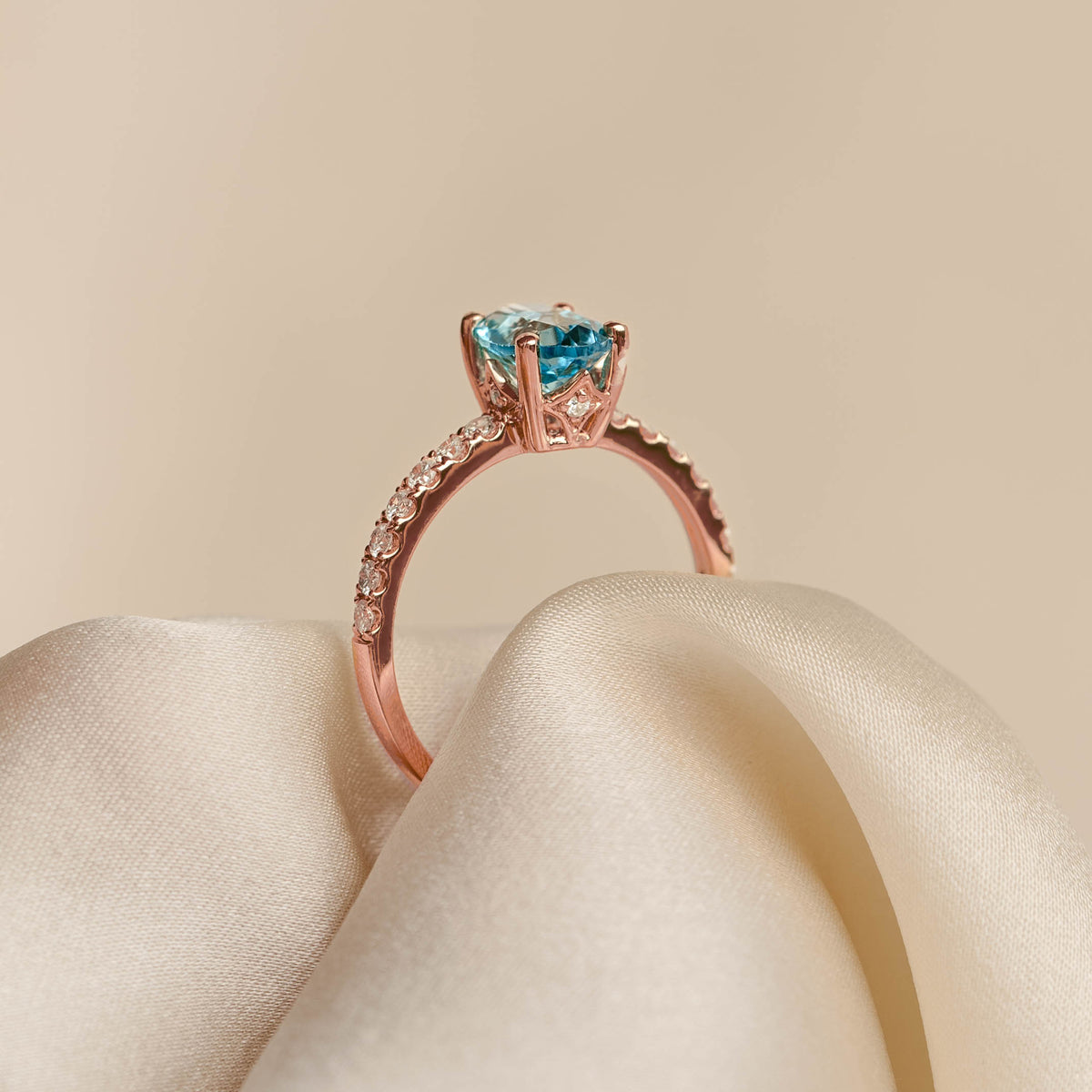 Oval Swiss Blue Topaz and Diamond Ring Rose Gold - Minette resting on soft beige fabric with pavé diamond band details
