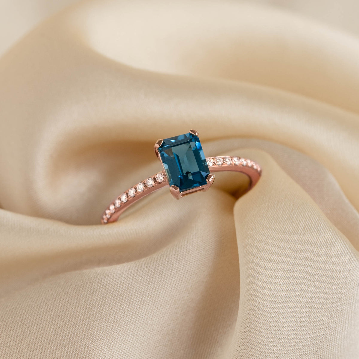Close-up of Baguette London Blue Topaz and Diamond Ring Rose Gold - Safiya on soft beige fabric background