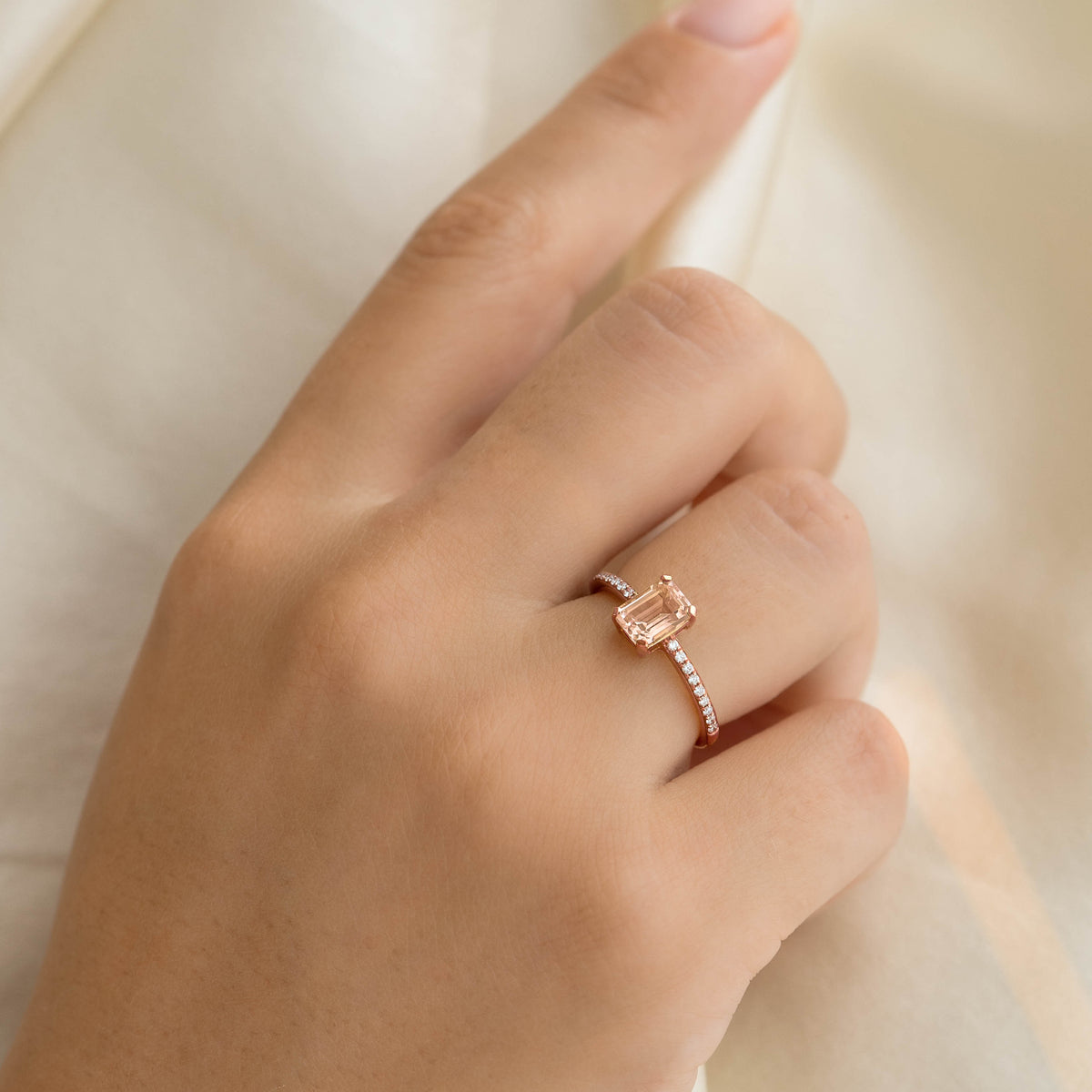 Close-up of hand wearing Baguette Morganite and Diamond Ring Rose Gold - Safiya on a soft cream fabric background
