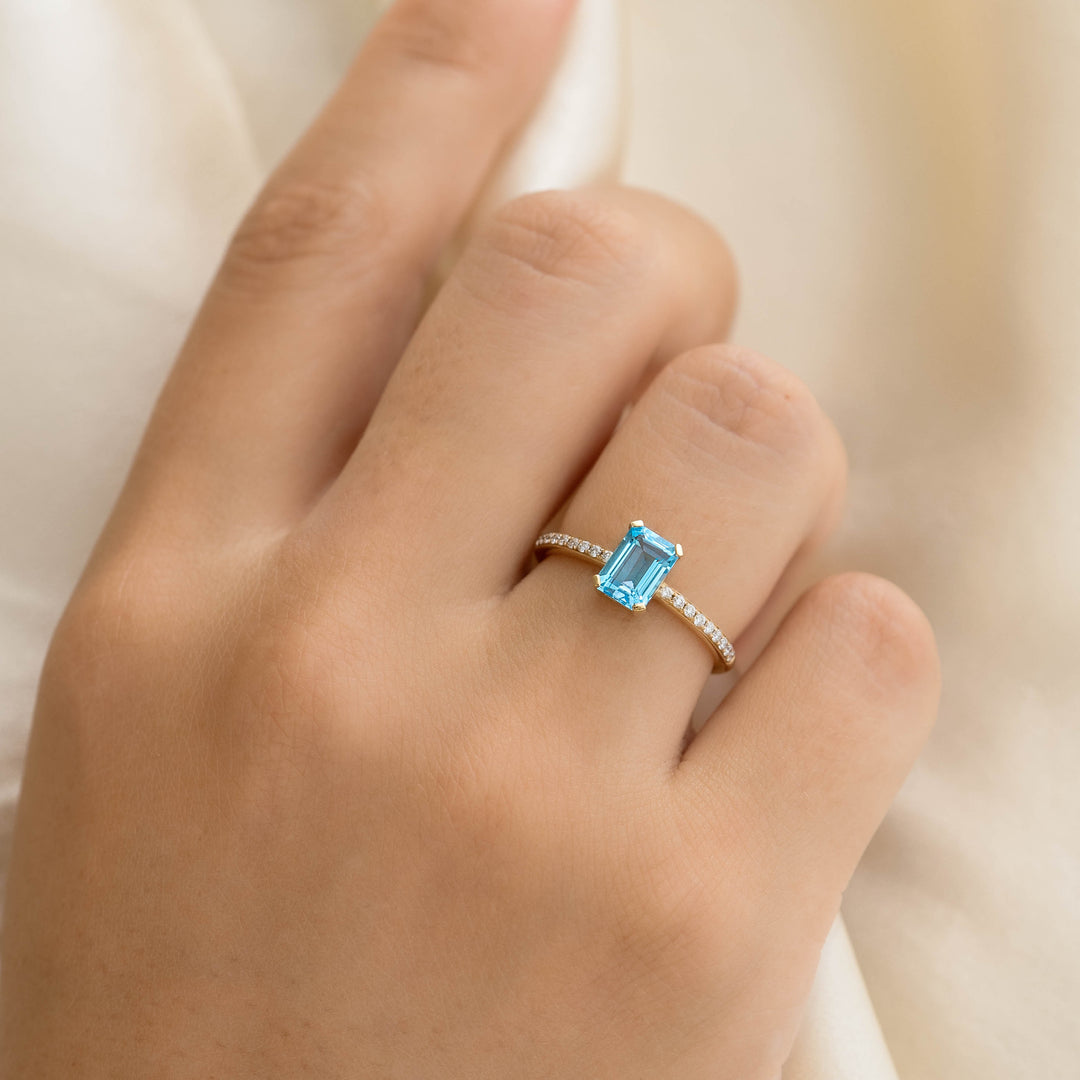 Close-up of a hand wearing Baguette Swiss Blue Topaz and Diamond Ring 14k Gold - Safiya with a light fabric background