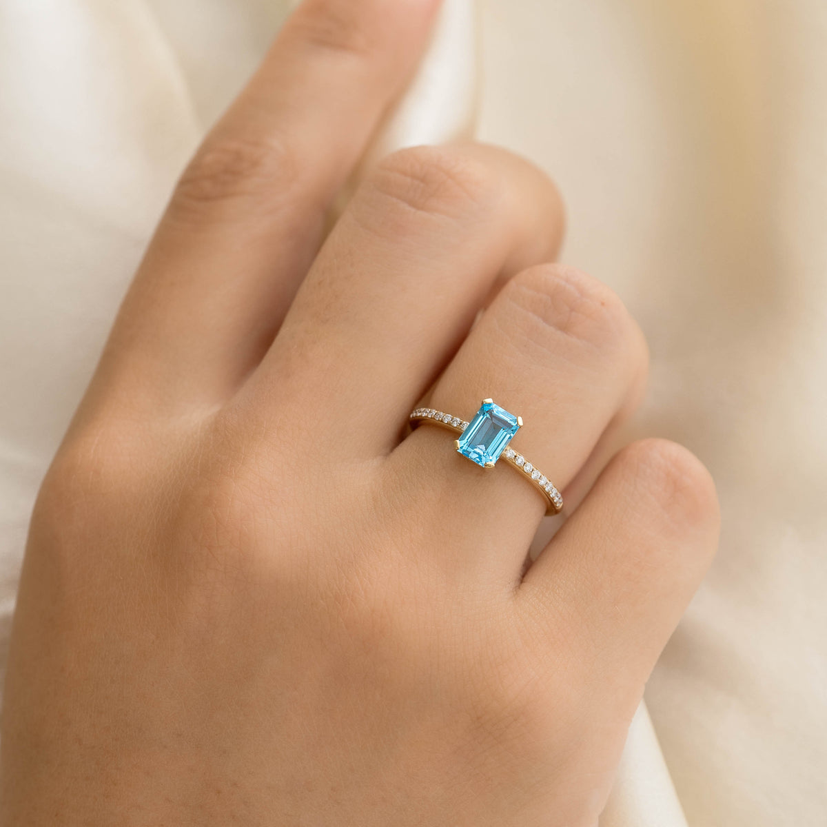 Close-up of a hand wearing Baguette Swiss Blue Topaz and Diamond Ring 14k Gold - Safiya with a light fabric background