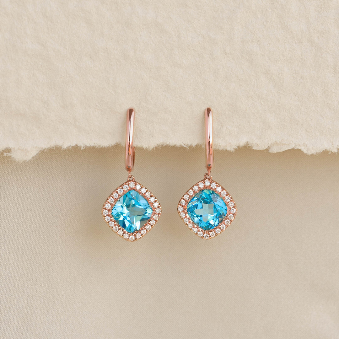 Swiss Blue Topaz and Diamond Halo Drop Earrings Rose Gold - Elvira with vibrant blue stones and sparkling diamond halo on beige background